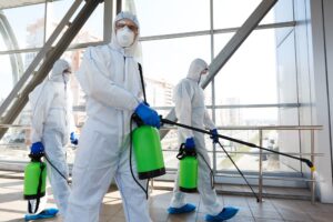 Professional workers in hazmat suits disinfecting indoor accommodation